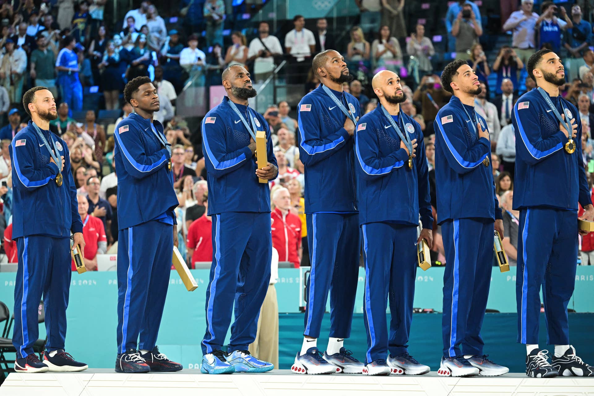 Gold medallists (From L) USA's #04 Stephen Curry, USA's #05 Anthony Edwards, USA's #06 LeBron James, USA's #07 Kevin Durant, USA's #08 Derrick White, USA's #09 Tyrese Haliburton and USA's #10 Jayson Tatum stand at attention during their national anthem, on the podium after the men's Gold Medal basketball match between France and USA during the Paris 2024 Olympic Games at the Bercy Arena in Paris on August 10, 2024. (Photo by Damien MEYER / AFP) (Photo by DAMIEN MEYER/AFP via Getty Images)