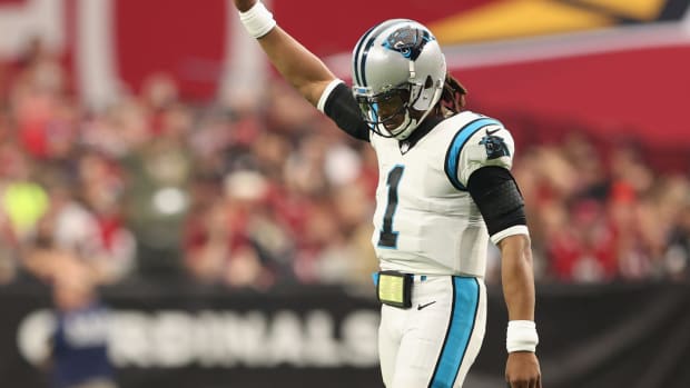 Cam Newton lifts his right arm in the air while on the field during a game.