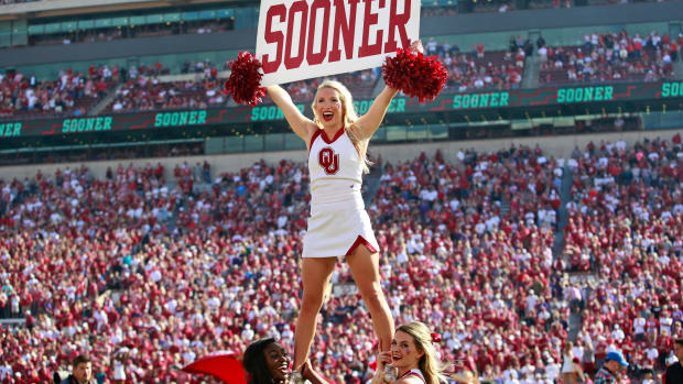 A photo of an Oklahoma cheerleader holding up a sign that says "Sooner" during a football game.