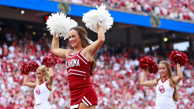 Three Oklahoma Sooners cheerleaders waving pompoms during a football game.
