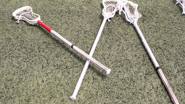 Three lacrosse sticks stacked on the ground.