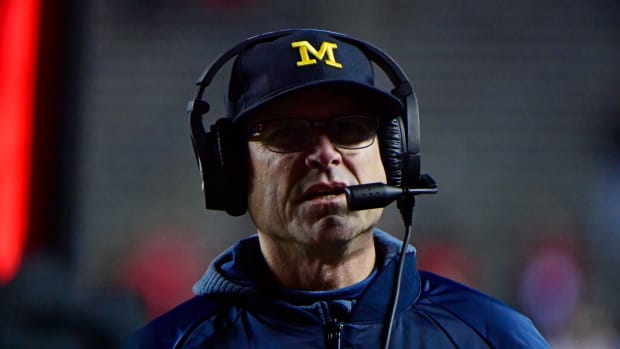 A closeup of Michigan college football head coach Jim Harbaugh wearing a Michigan hat and jacket.