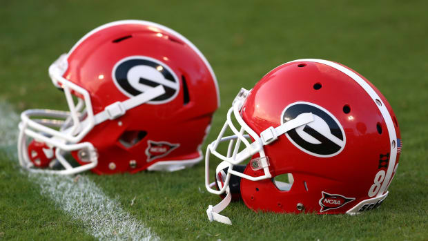 Two Georgia football helmets sitting on a field.