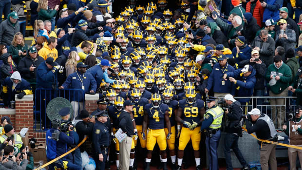 Head coach Jim Harbaugh of the Michigan Wolverines leads his Michigan football team onto the field before the college football game against the Michigan State Spartans.