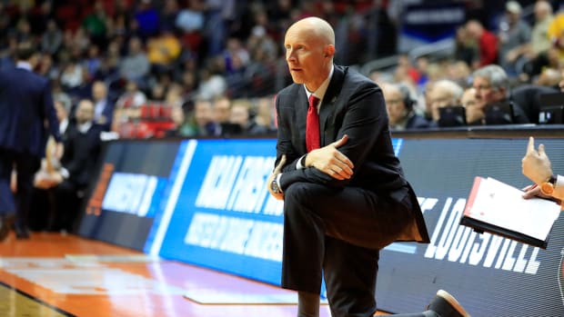 Louisville Cardinals head coach Chris Mack kneeling on the sideline during a game.
