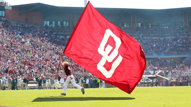 A man running with an Oklahoma Sooners flag during a football game.