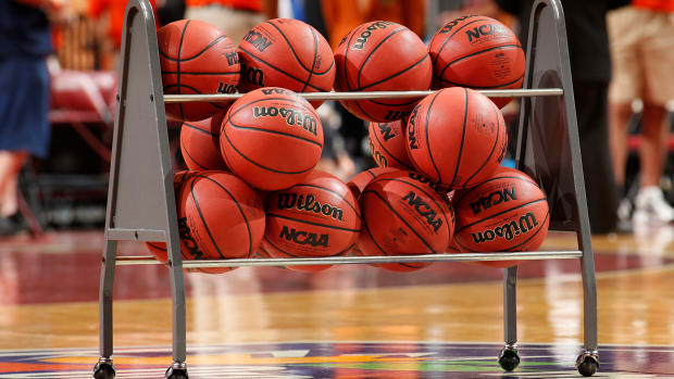 NCAA basketballs sitting in a ball rack on the court.