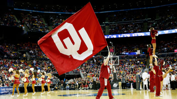 An Oklahoma Sooners cheerleader holding up an Oklahoma flag.