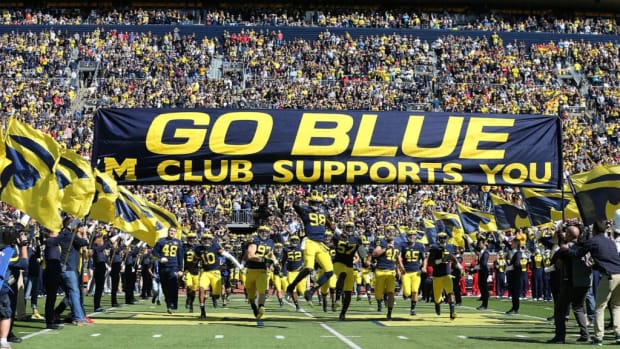Michigan football players run under the "Go Blue" banner before a home game.