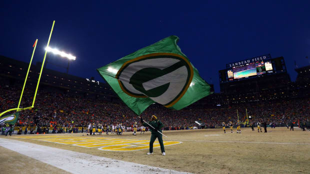 A man waving a Green Bay Packers flag at Lambeau Field.