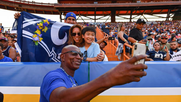 Eric Dickerson smiles and takes a selfie with Rams fans at a game.