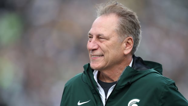 A closeup of Michigan State college basketball coach Tom Izzo wearing a green Michigan State jacket during a football game.