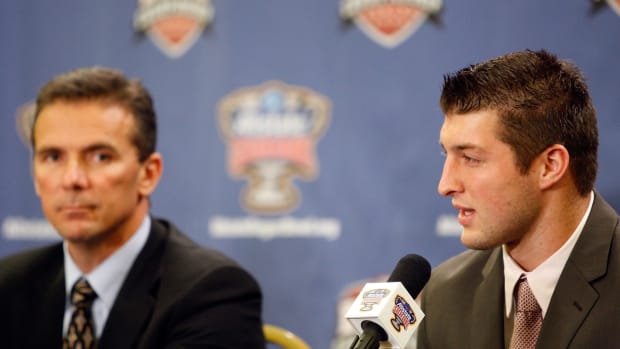 Tim Tebow speaking at a press conference with Urban Meyer by his side.