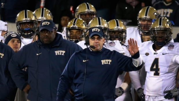 Pat Narduzzi holding his left hand up while his players stand behind him.