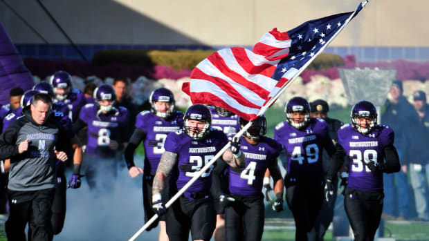 Northwestern football player leading his team onto the field while holding an American flag.
