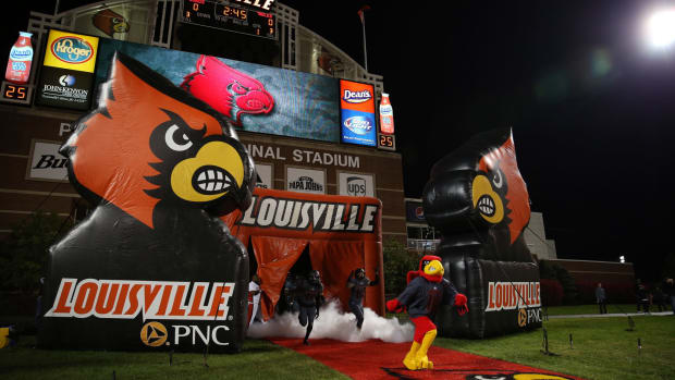 Louisville's mascot leads the football team on the field.