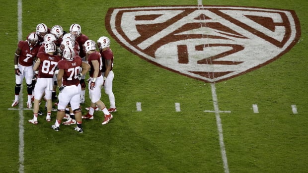 Stanford's football team huddled up on the field next to a PAC-12 logo.