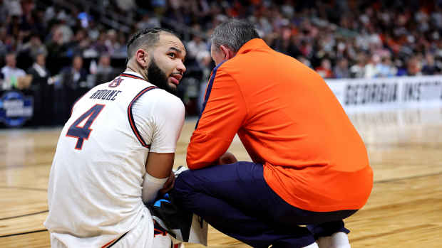 Johni Broome sits on the floor with a trainer after getting injured.