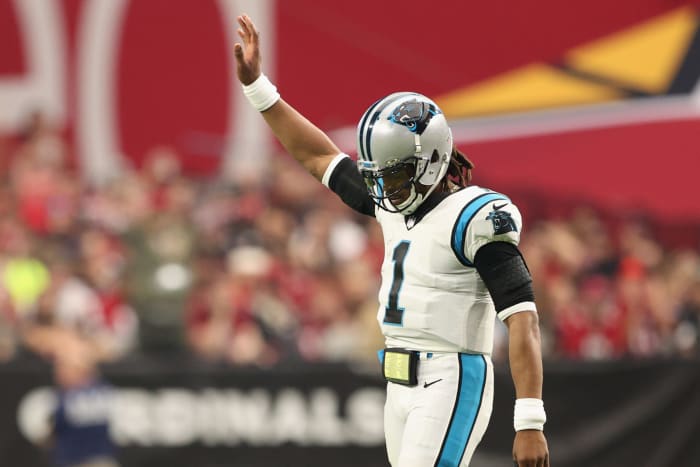 Cam Newton lifts his right arm in the air while on the field during a game.