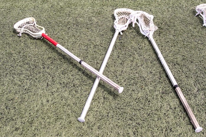 Three lacrosse sticks stacked on the ground.