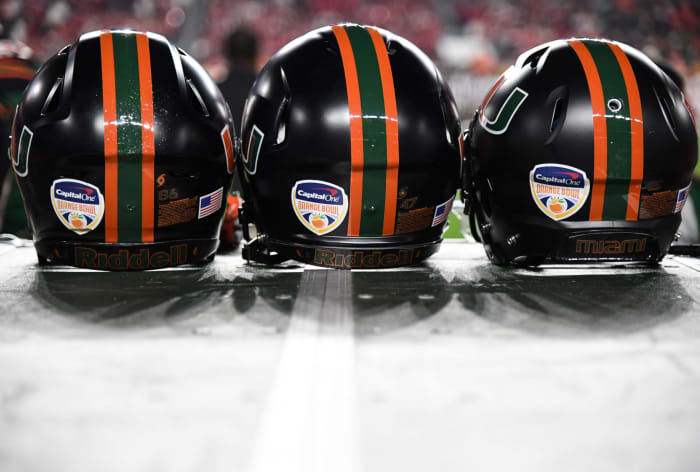 A closeup of Miami football helmets sitting on a bench.