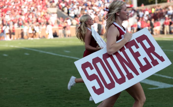 An Oklahoma cheerleader holding up a Sooner sign during a football game.