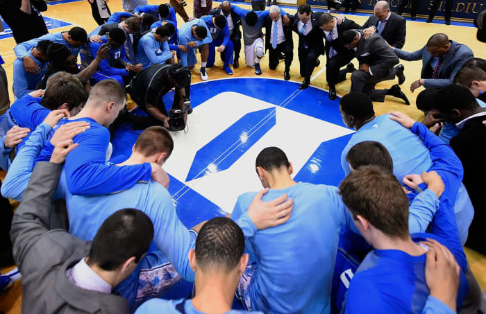 Duke and North Carolina players and coaches kneel at half court.