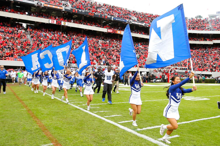 Kentucky cheerleaders run on the field with flags.