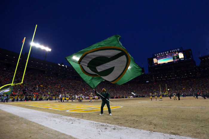 A man waving a Green Bay Packers flag at Lambeau Field.
