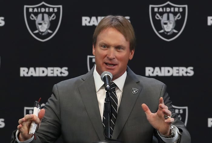 Jon Guden addressing the media in front of a Raiders backdrop.