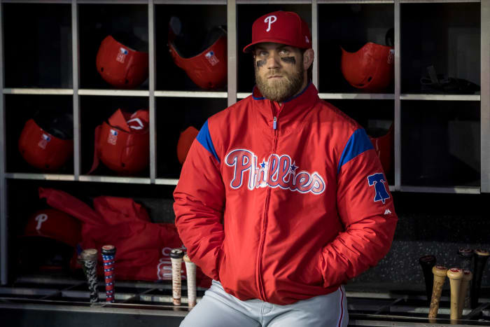 Bryce Harper standing in the dugout wearing his Phillies jacket.