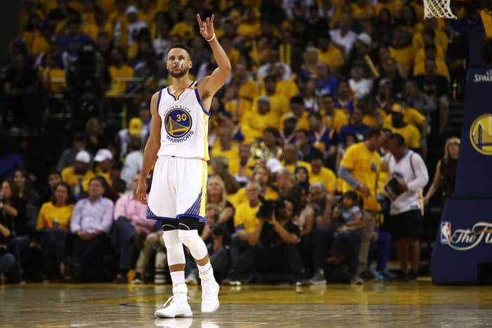 Steph Curry looking into the crowd with his left hand up.