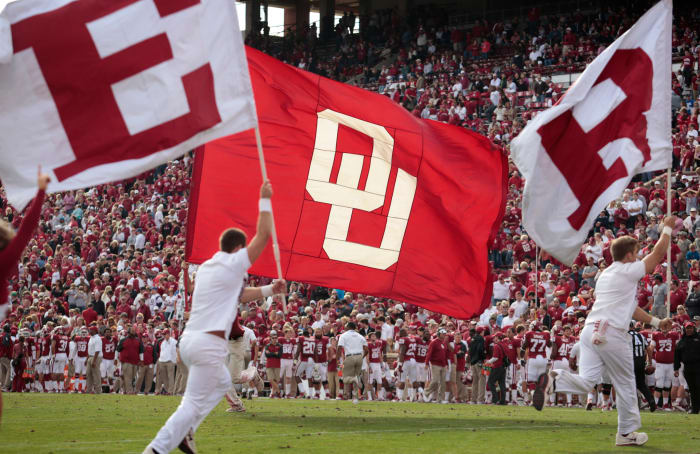 Oklahoma cheerleaders running with flags in their hands.