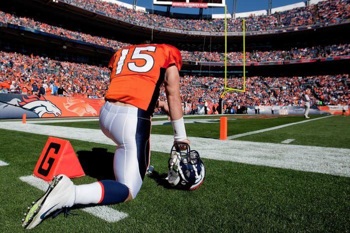 Tim Tebow kneeling on the football field in his Denver Broncos uniform.