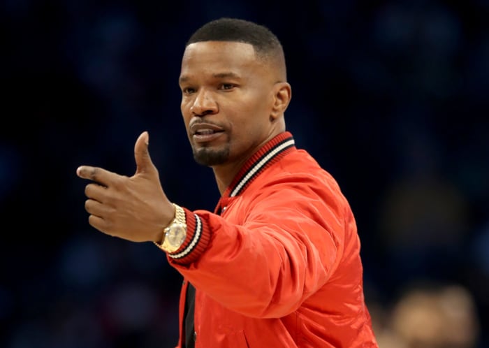 A closeup of Jamie Foxx wearing a red jacket at the NBA All-Star game.