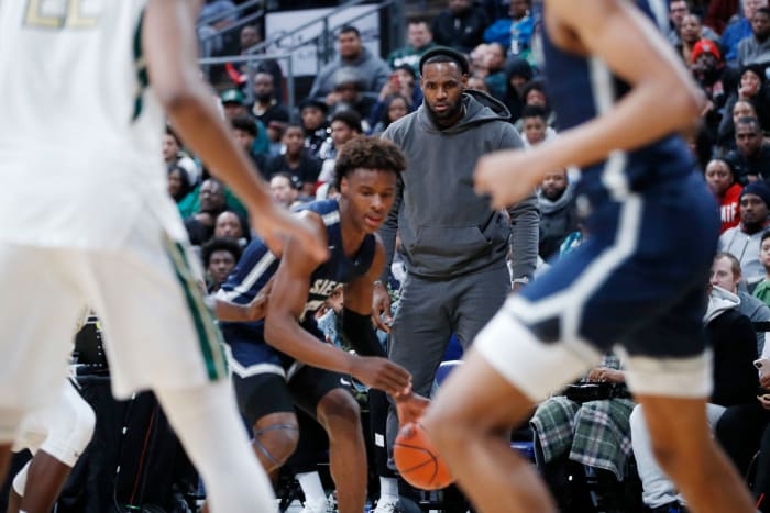 Bronny James plays in a high school game as LeBron James looks on.