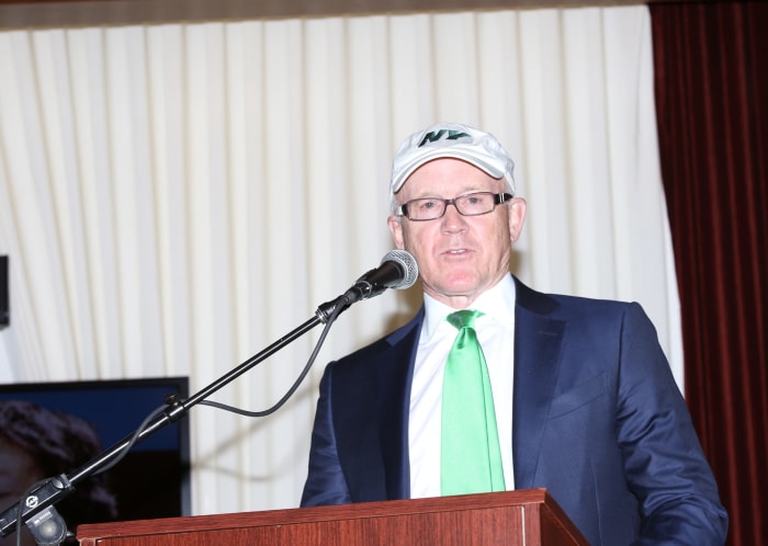 New York Jets owner Woody Johnson speaking at a podium.