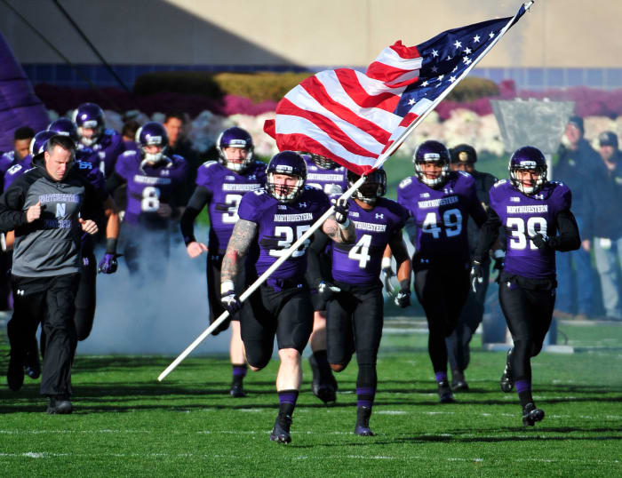 Northwestern football player leading his team onto the field while holding an American flag.