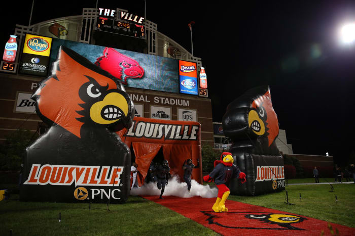 Louisville's mascot leads the football team on the field.