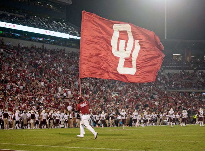 An Oklahoma cheerleader running with an OU flag.