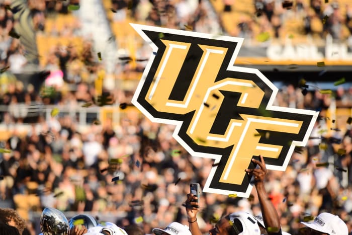 UCF Football players holding a UCF football sign in the air.