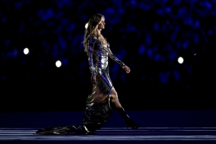 Gisele Bundchen walking in a long dress at the Olympics.