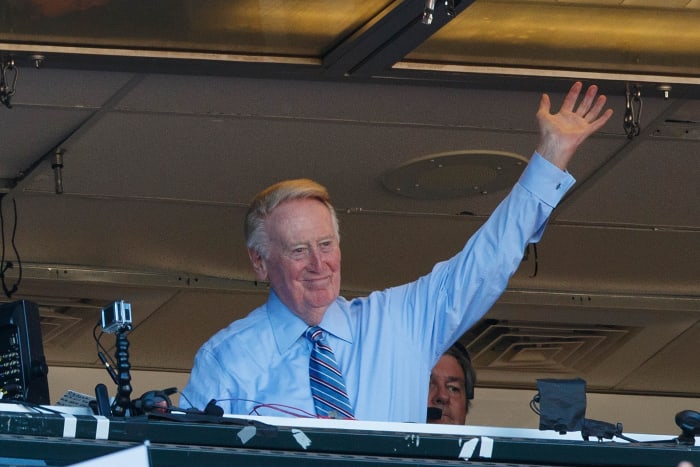 Legendary announcer Vin Scully points to the crowd during a playoff game.