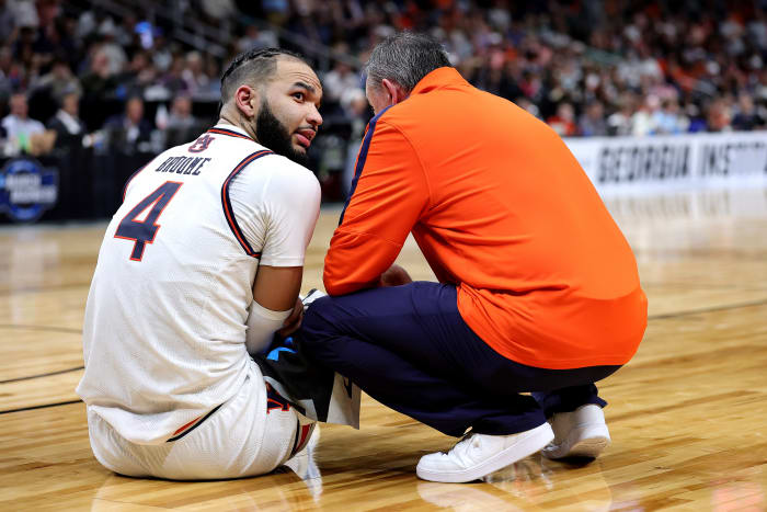 Johni Broome sits on the floor with a trainer after getting injured.