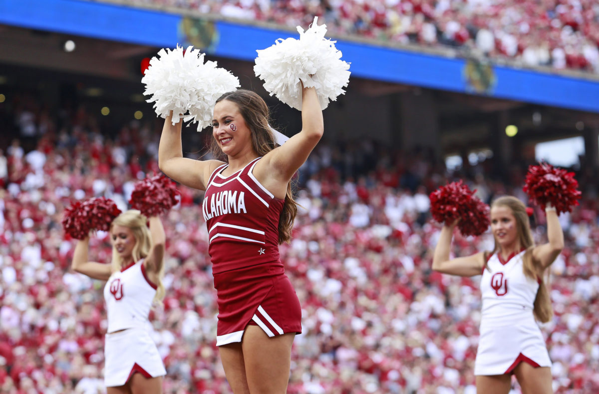 Three Oklahoma Sooners cheerleaders waving pompoms during a football game.