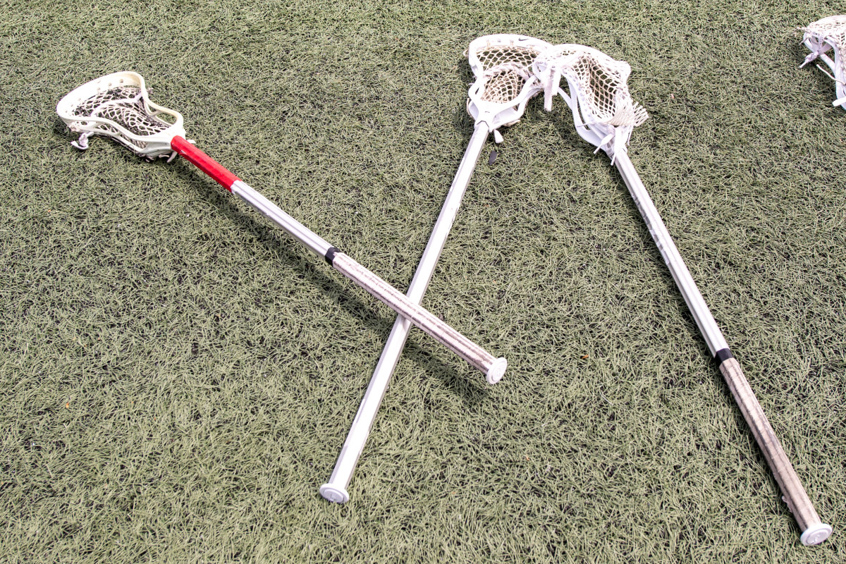 Three lacrosse sticks stacked on the ground.