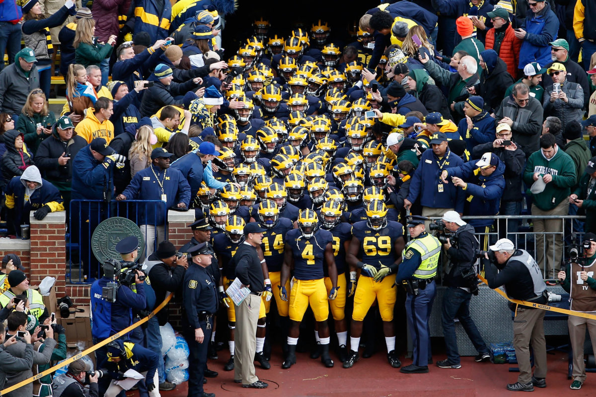 Head coach Jim Harbaugh of the Michigan Wolverines leads his Michigan football team onto the field before the college football game against the Michigan State Spartans.
