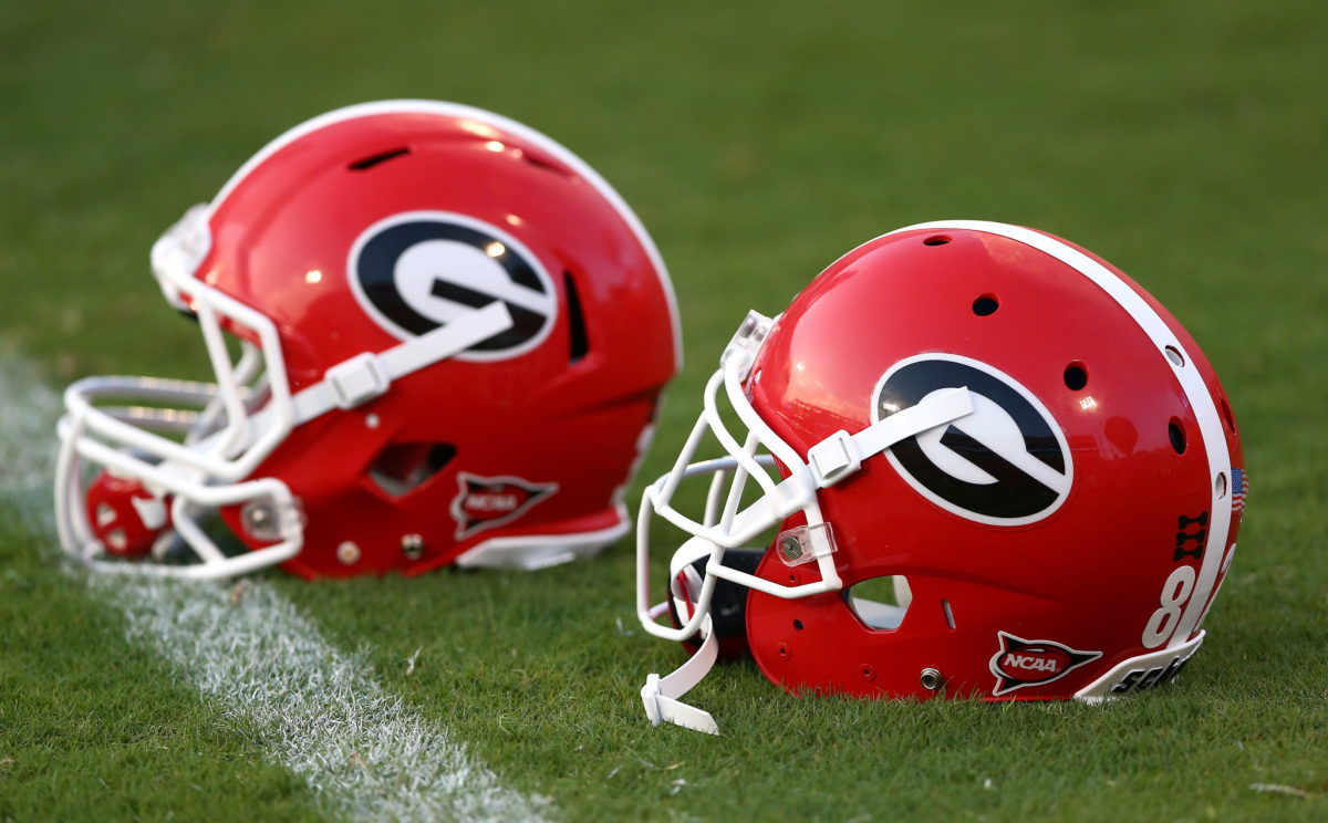 Two Georgia football helmets sitting on a field.