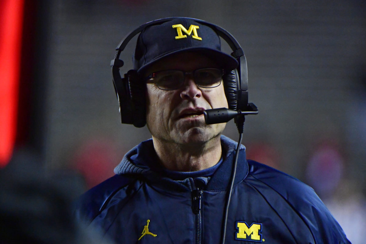 A closeup of Michigan college football head coach Jim Harbaugh wearing a Michigan hat and jacket.