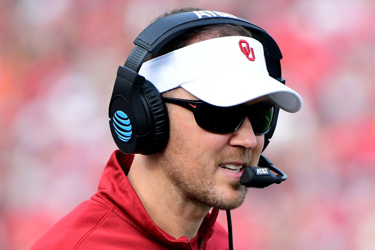A closeup of Lincoln Riley wearing an Oklahoma Sooners visor and a headset.